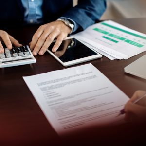 Close-up of financial consultant using calculator while his client is signing paperwork during the meeting.