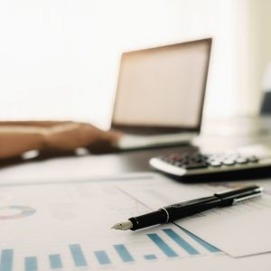 Business concept with copy space. Office desk table with pen focus and analysis chart, computer, notebook, cup of coffee on desk.Vintage tone Retro filter, selective focus.